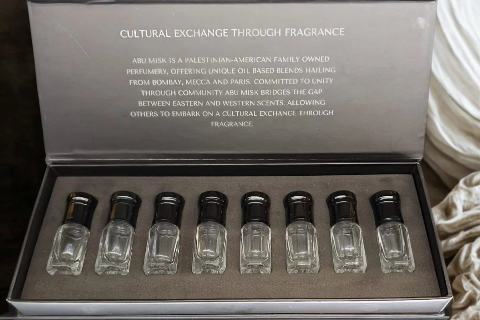 Set of small glass bottles with black caps in a gray box on a textured surface.