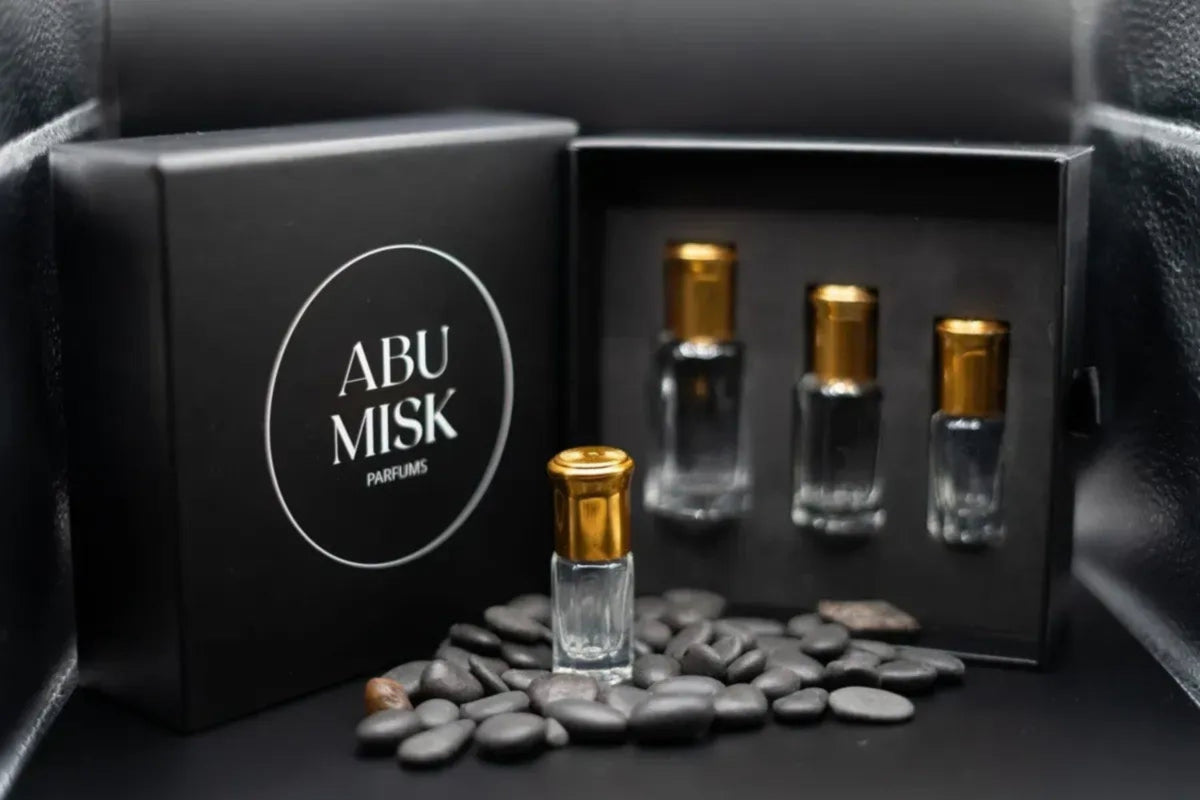 Set of Abu Misq perfume bottles in a black box with pebbles on a dark surface