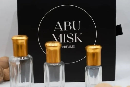 Three Abu Misq perfume bottles with a black box in the background on a white surface.