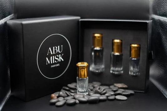 Set of Abu Misq perfume bottles in a black box with pebbles on a dark surface